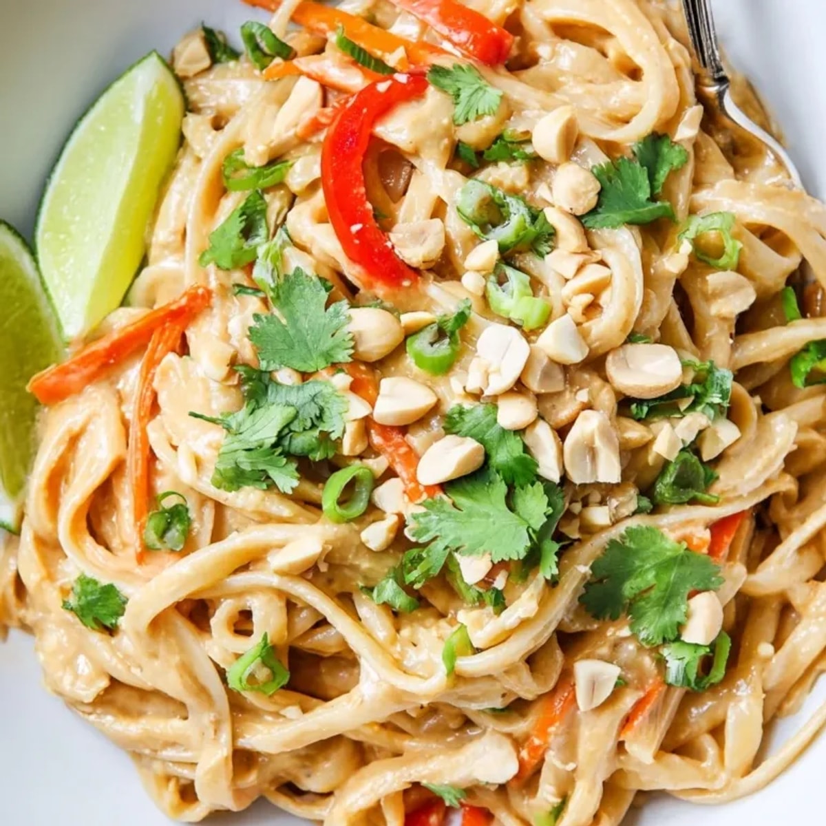 Close-up: Stirring savory Creamy Peanut Butter Noodles in a bowl with sesame seeds.
