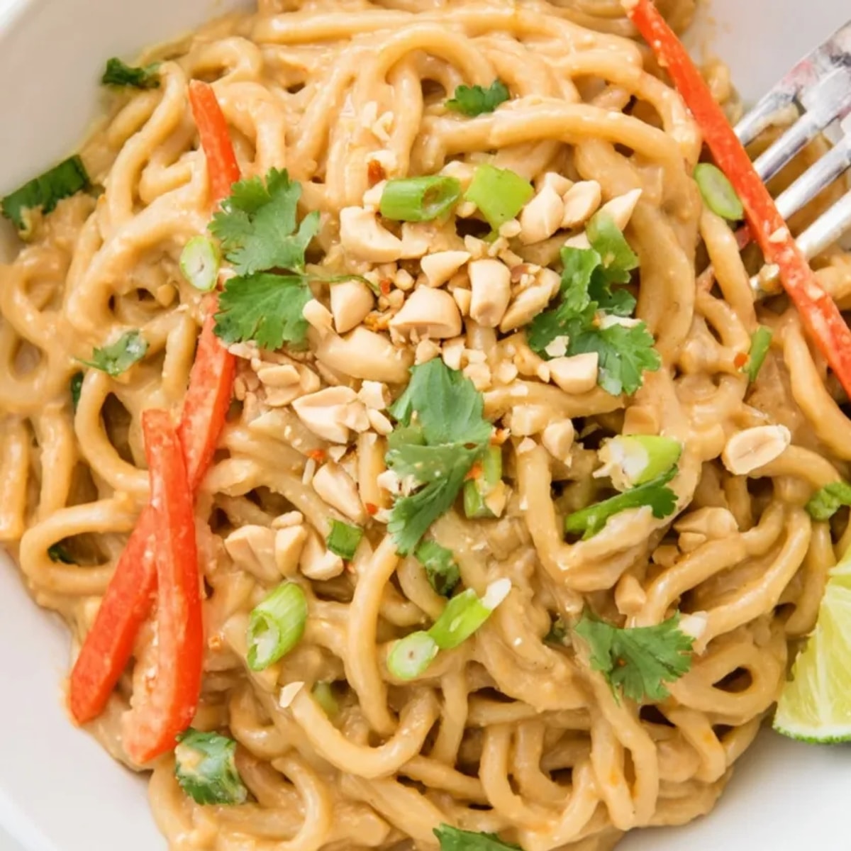 Overhead view: Creamy Peanut Butter Noodles glistening, topped with vibrant carrot and cilantro.