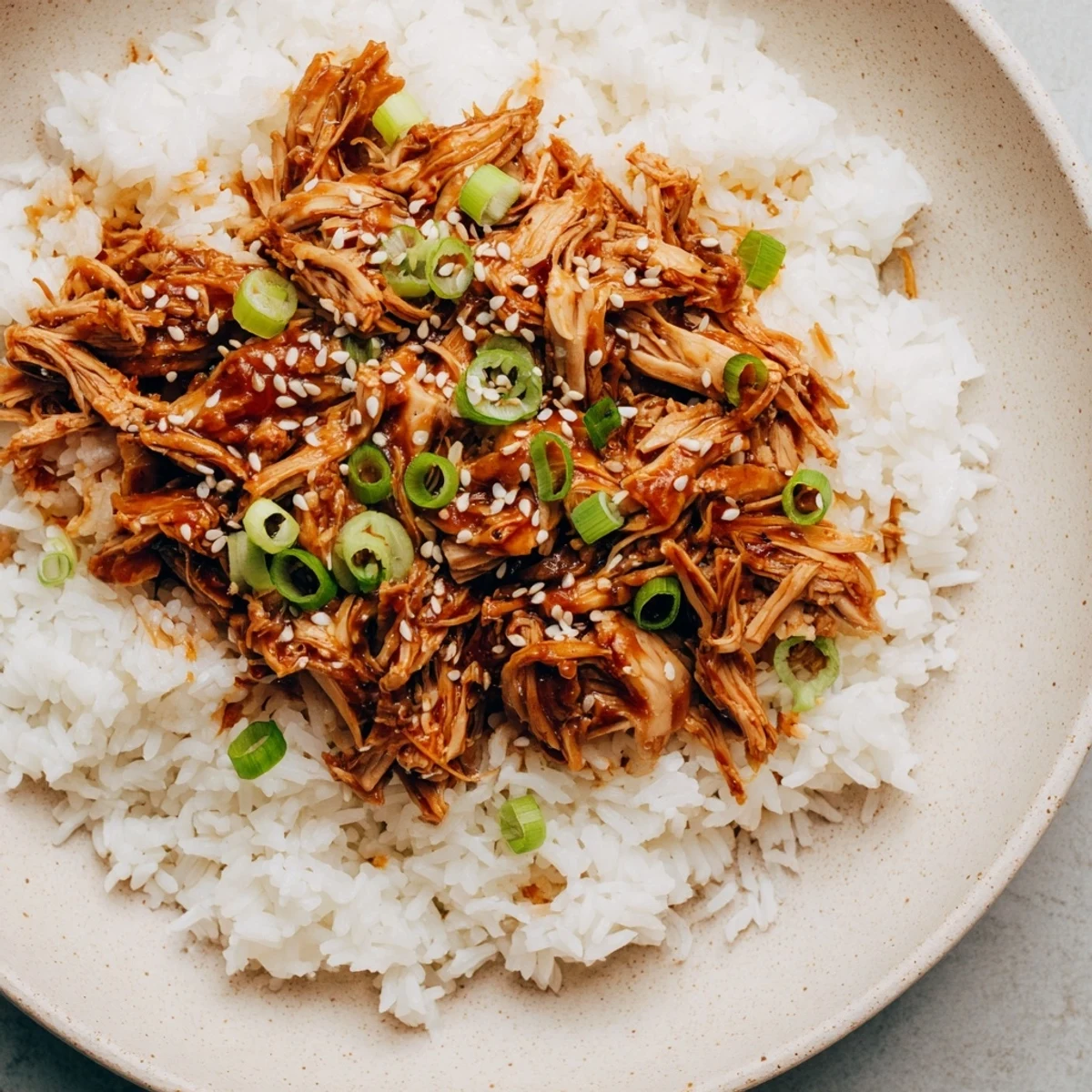 A steaming bowl of Easy Slow Cooker Teriyaki Chicken with rice, garnished with green onions and sesame seeds.