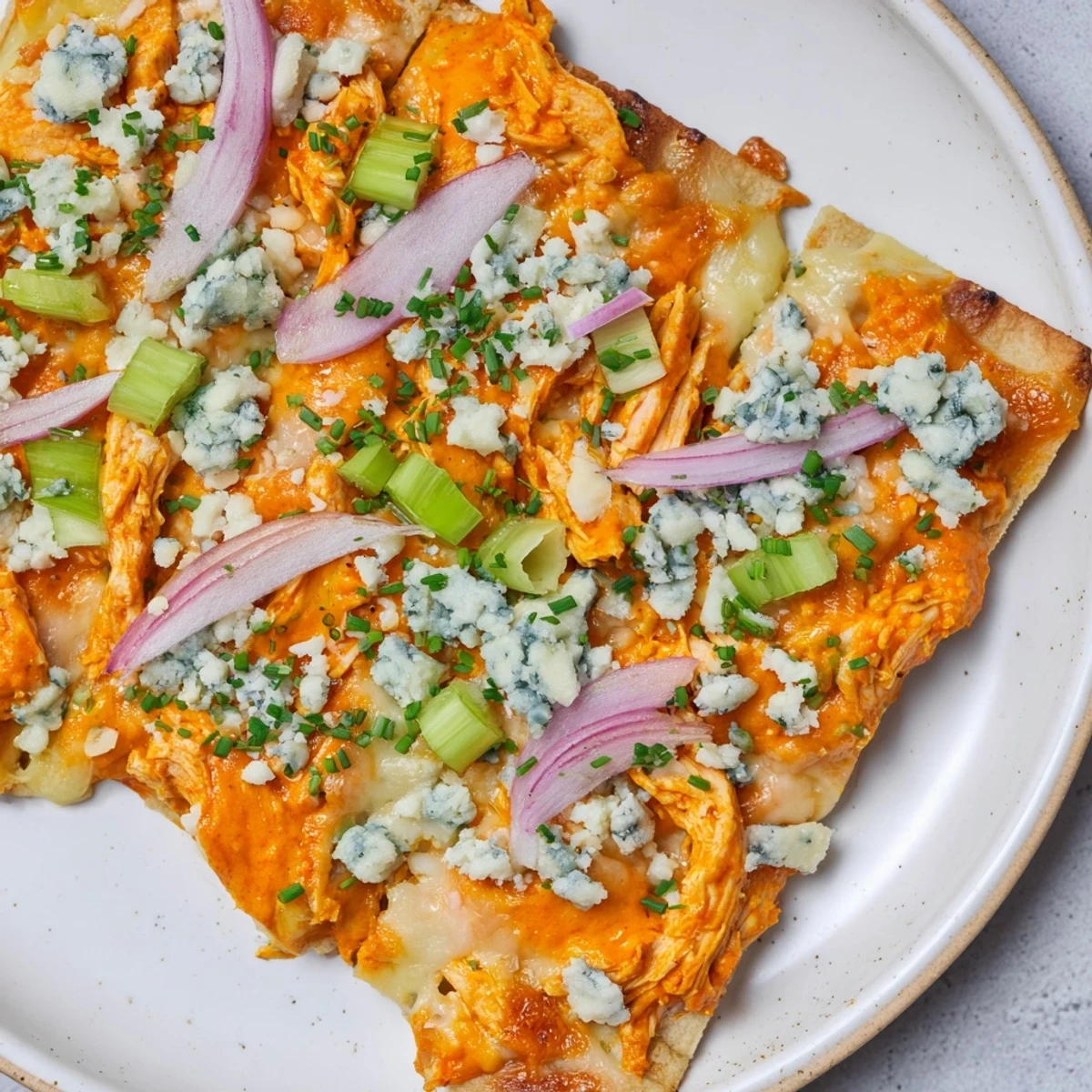 Crispy-edged Buffalo Chicken & Blue Cheese Flatbread topped with vibrant red onion and crumbled blue cheese.
